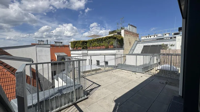 Geräumige Dachterrasse mit Fliesenboden, Metallgeländer und weitem Blick über die umliegenden Dächer.
