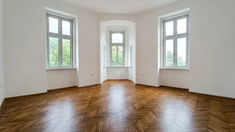 Helles Zimmer mit Fischgrätparkett und Erkerfenstern, ideal für Wohn- oder Schlafbereich.