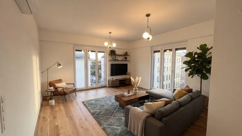 Helles, modern eingerichtetes Wohnzimmer mit Holzboden, großen Fenstern und Klimaanlage.