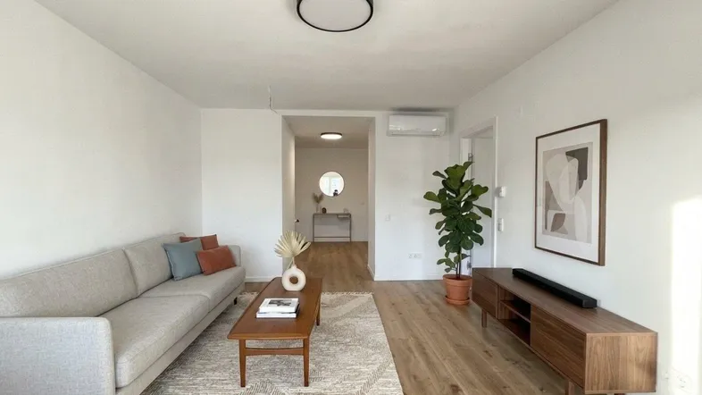 Helles Wohnzimmer mit modernem Sofa, Holzboden und Blick in den Flur.