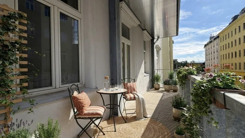 Heller Balkon mit gemütlicher Sitzgelegenheit, Pflanzen und Blick auf die Stadt.