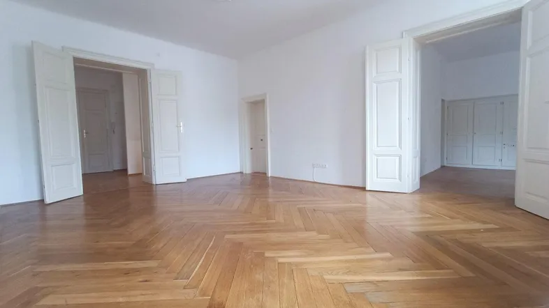 Helles Zimmer mit Fischgrätparkett, hohen Decken und dekorativem Deckenstuck, bereit zum Einzug.
