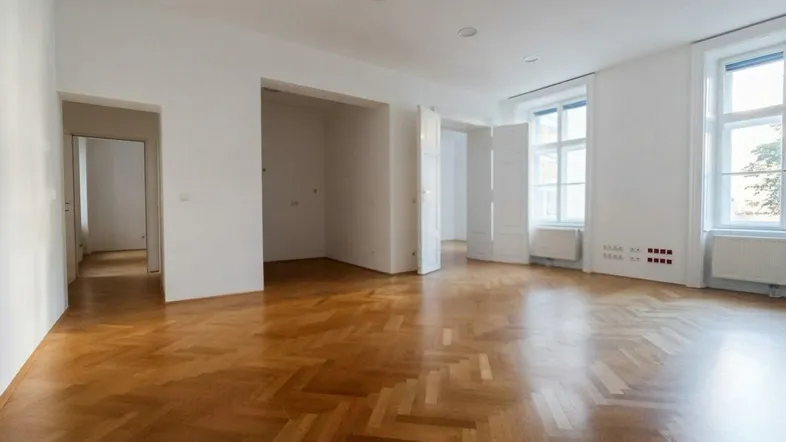 Helles Wohnzimmer mit Fischgrätparkett, hohen Decken und mehreren Türen, bereit zum Einzug.