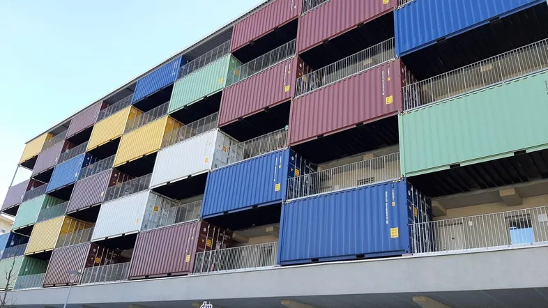 Moderne Gebäudefassade mit bunten Schiffscontainern als Balkonelemente und innovativer Architektur.
