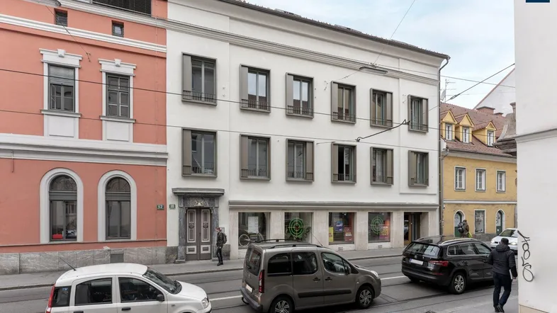 Historisches Gebäude mit klassischer Fassade und Geschäften im Erdgeschoss an einer belebten Straße.