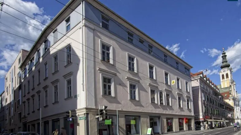 Historisches Eckgebäude in der Stadt mit mehreren Stockwerken und Geschäften im Erdgeschoss.