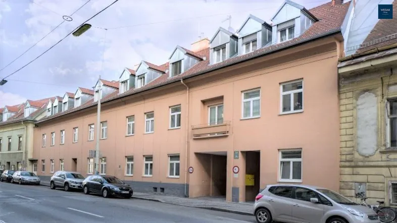 Gebäudefassade mit mehreren Fenstern und Dachgauben an einer Straße mit parkenden Autos.