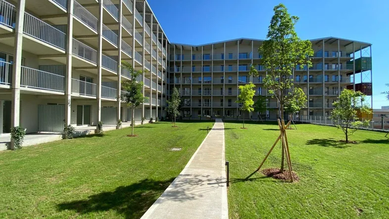 Moderne Wohnanlage mit vielen Balkonen, gepflegtem Rasen und einem Gehweg unter blauem Himmel.