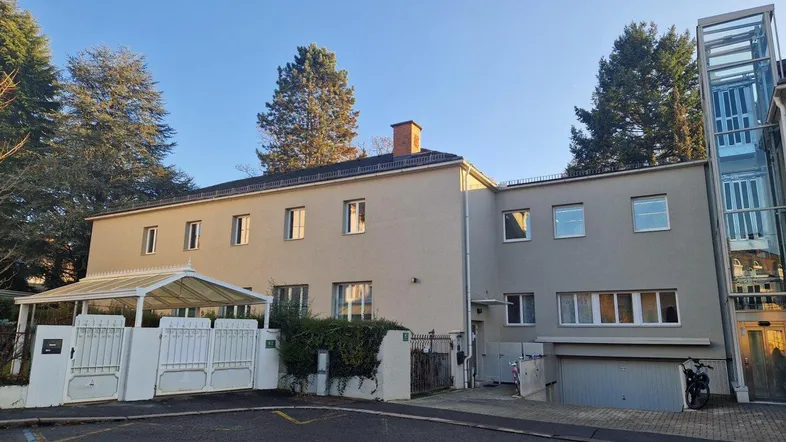 Mehrstöckiges Gebäude mit moderner Fassade, großen Fenstern und einem externen Glasaufzug.