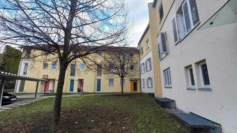 Mehrere Wohngebäude mit gelber Fassade und einem begrünten Innenhof mit Bäumen und Parkplätzen.