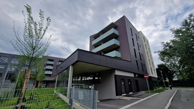 Modernes Mehrfamilienhaus mit dunkler Fassade, Balkonen und Tiefgaragenzufahrt unter bewölktem Himmel.