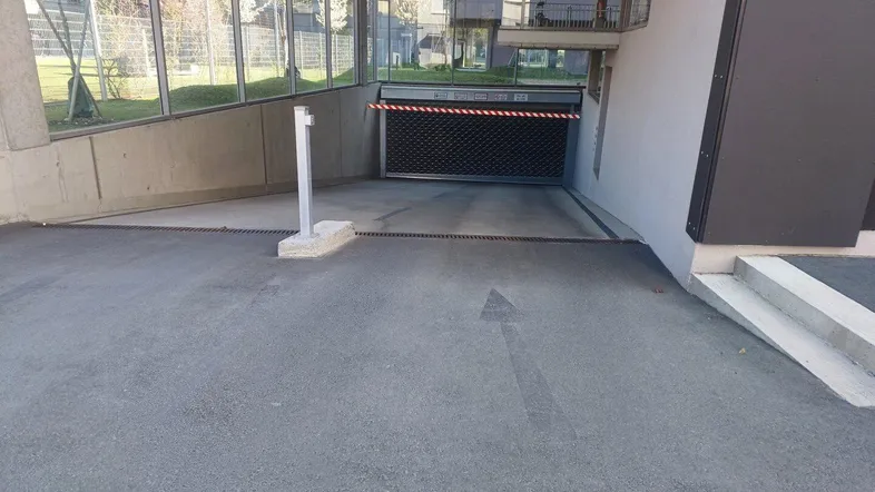 Einfahrt zur Tiefgarage eines modernen Gebäudes mit Schranke und Rolltor.