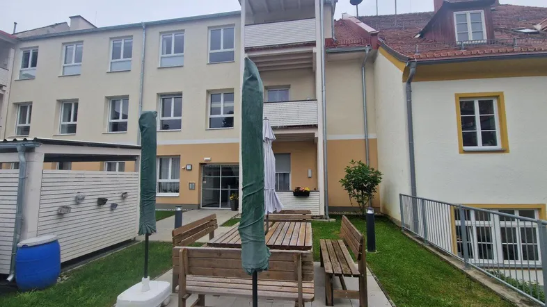 Außenansicht des Gebäudes mit einem kleinen Gartenbereich und Sitzgelegenheiten im Freien.