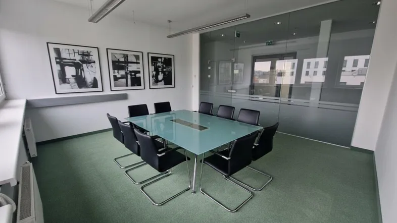 Moderner Konferenzraum mit Glastrennwand, Teppichboden und Blick nach draußen durch große Fenster.