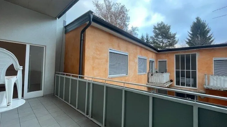 Geräumiger Balkon mit Fliesenboden und Blick auf umliegende Gebäude und Bäume.
