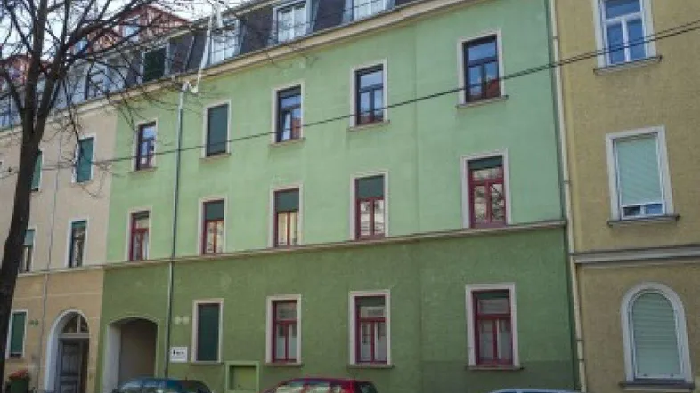 Fassade eines Mehrfamilienhauses mit grüner Farbgebung und klassischen Fenstern in städtischer Umgebung.