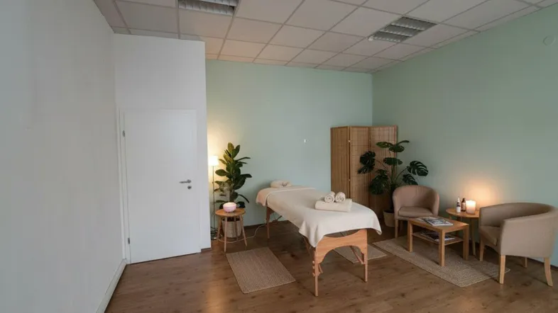 Heller Raum mit Holzboden, Massageliege und Pflanzen, ideal für Therapie oder Büro.