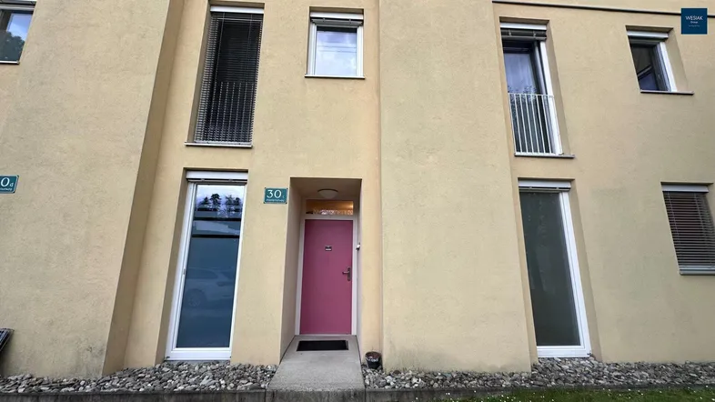 Fassade eines modernen Wohngebäudes mit einer auffälligen pinken Eingangstür und Fenstern.
