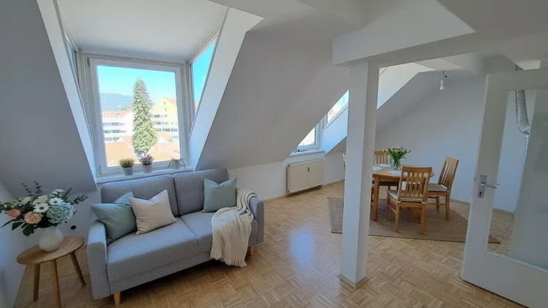 Heller Wohn- und Essbereich im Dachgeschoss mit großen Fenstern, Parkettboden und Bergblick.