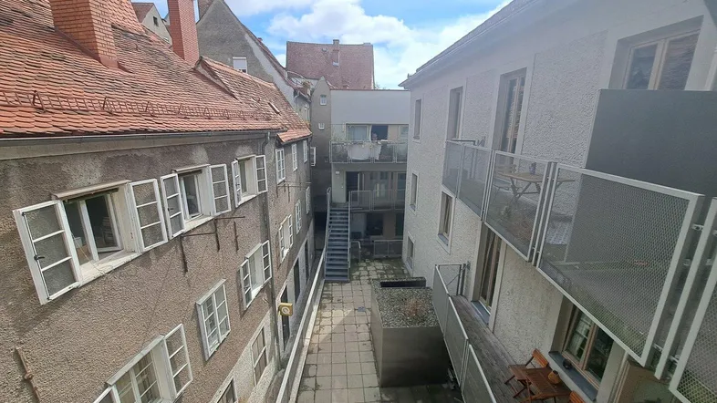 Blick auf einen ruhigen Innenhof, umgeben von Gebäuden mit Balkonen und traditionellen Dächern.