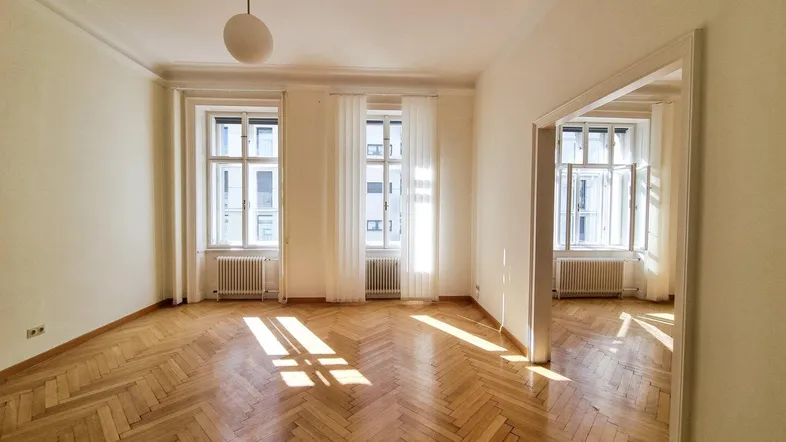 Helles Wohnzimmer mit Fischgrätparkett, hohen Decken und großen Fenstern, die viel Tageslicht hereinlassen.