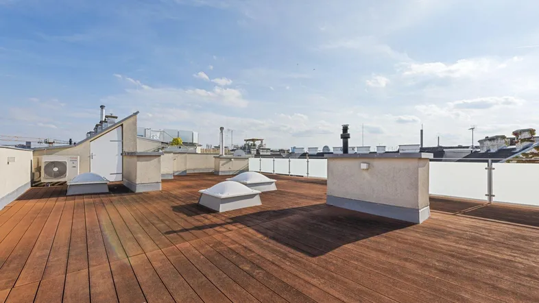 Geräumige Dachterrasse mit Holzboden, Glasgeländer und weitem Blick über die Stadt.