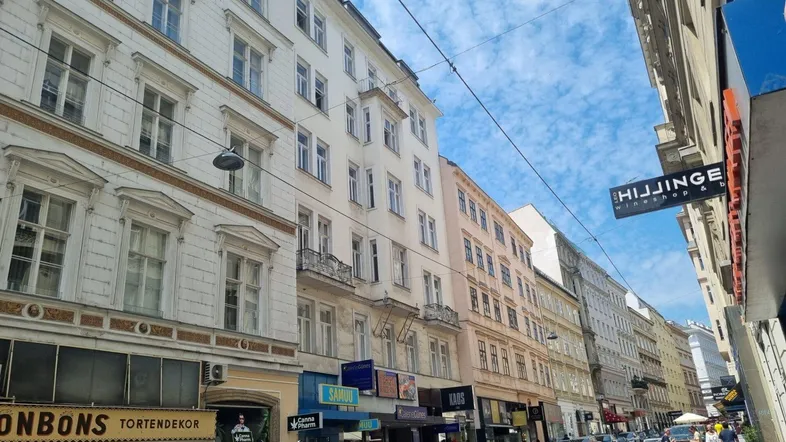 Historische Gebäudezeile in einer belebten Stadtstraße mit Geschäften im Erdgeschoss und Wohnungen darüber.