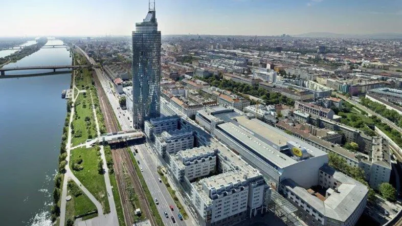 Luftaufnahme eines modernen Wolkenkratzers und umliegender Gebäude entlang eines Flusses in einer Stadt.