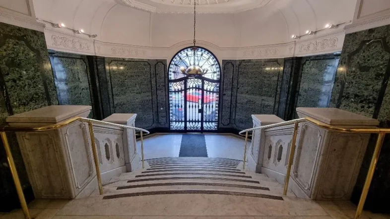 Prunkvolle Eingangshalle mit einer eleganten Marmortreppe, grünen Marmorwänden und einer verzierten Decke.