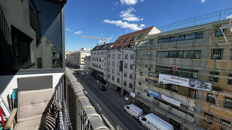 Blick vom Balkon auf die belebte Straße mit Gebäuden und einer Baustelle unter blauem Himmel.