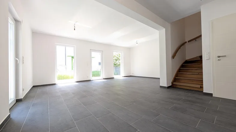 Geräumiges, helles Wohnzimmer mit modernem Fliesenboden und Zugang zum Gartenbereich.