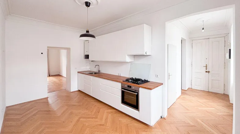 Helle Küche mit weißer Einbauküche, Holztheke und Fischgrätparkett, offen zu weiteren Räumen.