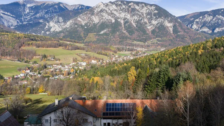 Ländliches Anwesen mit Solaranlage auf dem Dach, umgeben von Bergen und Wäldern.