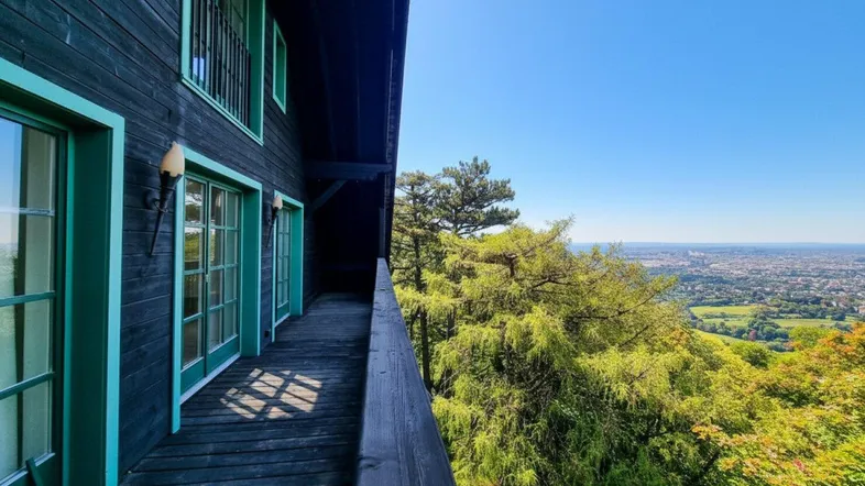 Langer Balkon mit Holzboden und Geländer, bietet einen weiten Blick über die Landschaft und die Stadt.