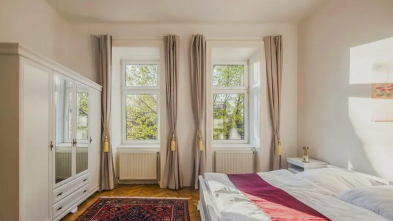 Helles Schlafzimmer mit Parkettboden, großem Kleiderschrank und Blick ins Grüne.