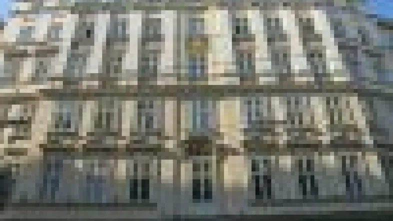 Die Fassade des Gebäudes zeigt klassische Architektur mit vielen Fenstern und mehreren Stockwerken.