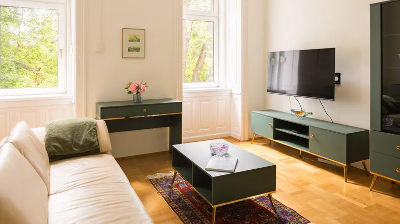 Helles Wohnzimmer mit Parkettboden, modernen Möbeln und Blick ins Grüne durch große Fenster.