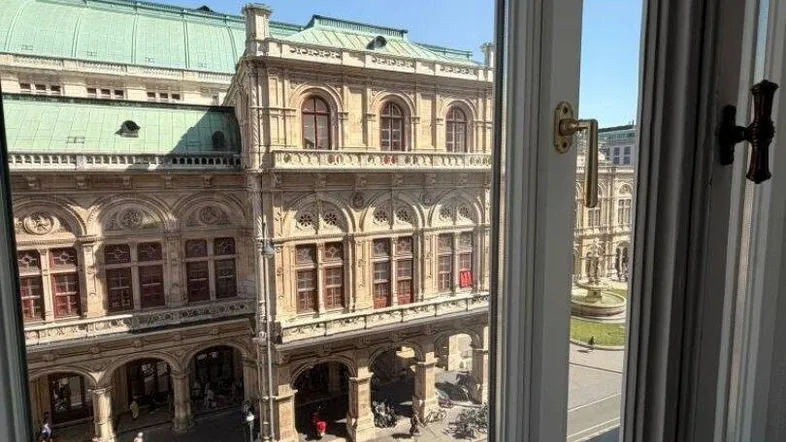 Blick aus dem Fenster auf ein prächtiges historisches Gebäude mit aufwendiger Architektur und einer belebten Straße.