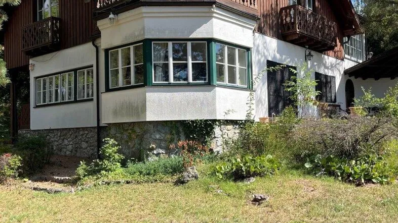 Traditionelles Haus mit mehreren Balkonen, grünen Fensterrahmen und umgebender Natur.