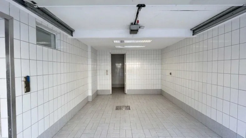 Geräumige, geflieste Garage mit automatischem Torantrieb und Zugang zu einem weiteren Raum im Hintergrund.