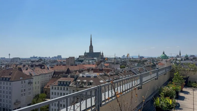 Große Dachterrasse mit Panoramablick über die Stadt Wien und historische Gebäude unter blauem Himmel.