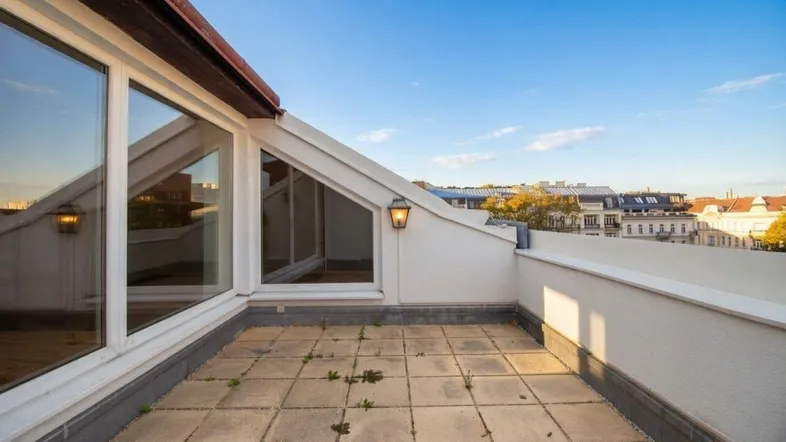 Geräumige Dachterrasse mit Fliesenboden und Blick auf die Stadt unter blauem Himmel.