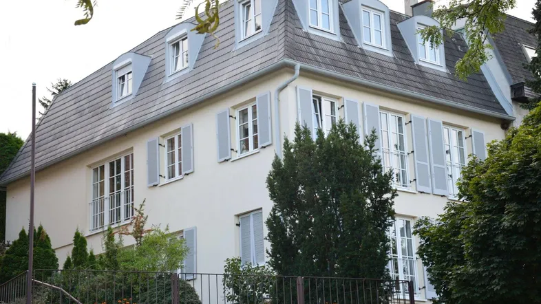 Klassisches Wohnhaus mit Mansarddach, hellen Fensterläden und gepflegter Fassade.