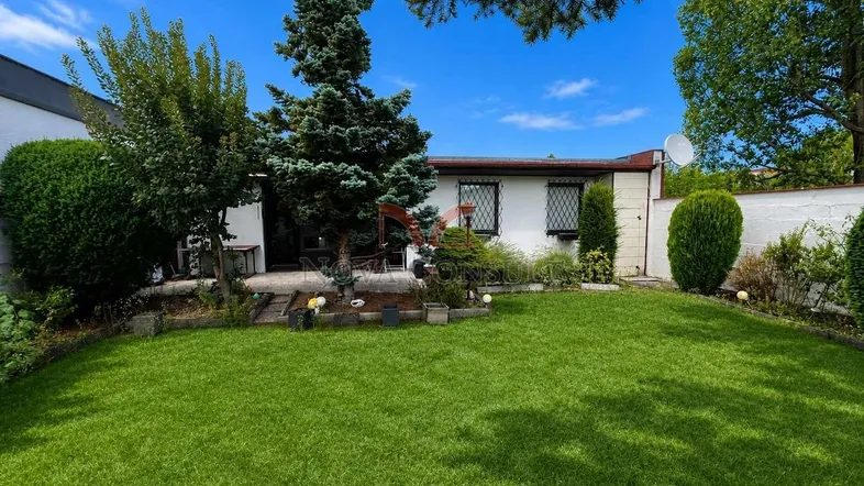 Gepflegter Garten mit weitläufiger Rasenfläche und kleiner Terrasse vor einem Einfamilienhaus.