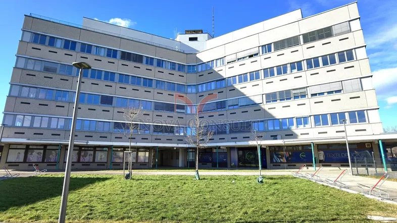 Großes Bürogebäude mit moderner Architektur und Grünfläche davor unter blauem Himmel.