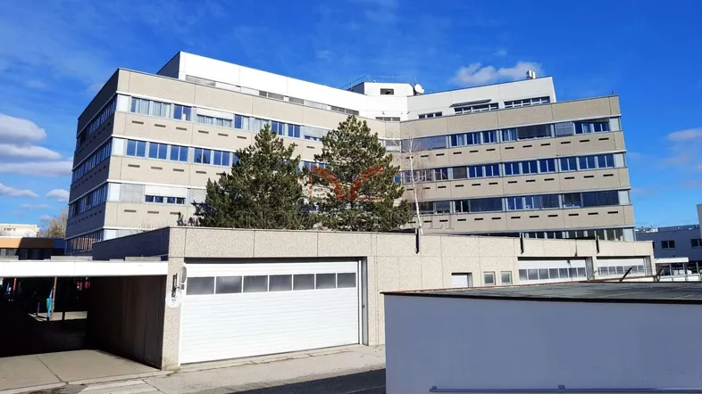Modernes Bürogebäude mit mehreren Etagen und einer Zufahrt zu einer Garage unter blauem Himmel.