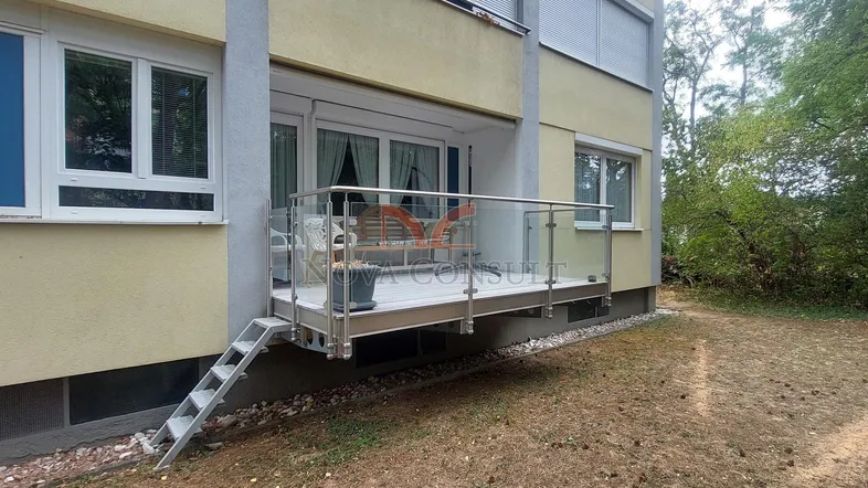 Moderne Terrasse mit Glasgeländer und Zugang zum Garten, ausgestattet mit Gartenmöbeln.