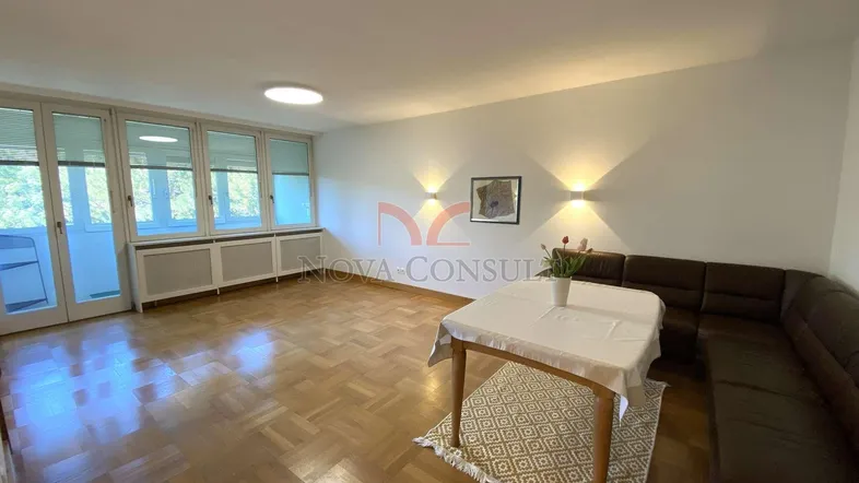 Helles Wohn- und Esszimmer mit Parkettboden, großen Fenstern und Zugang zu einem Balkon.