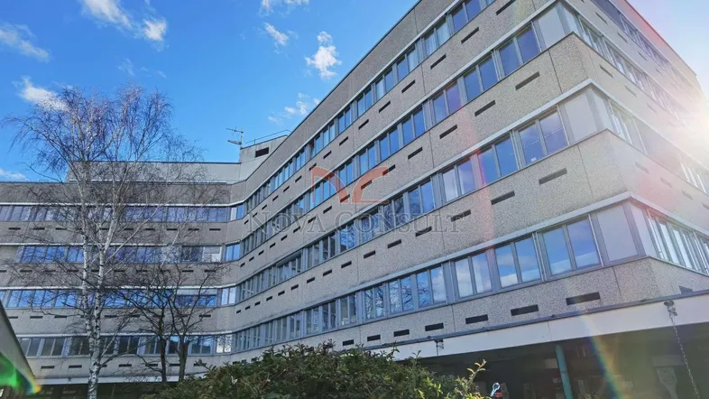 Mehrstöckiges Gebäude mit vielen Fenstern und einer modernen Betonfassade unter blauem Himmel.