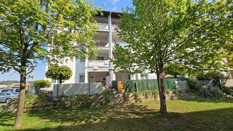 Mehrfamilienhaus mit gepflegter Grünfläche und Balkonen unter blauem Himmel.